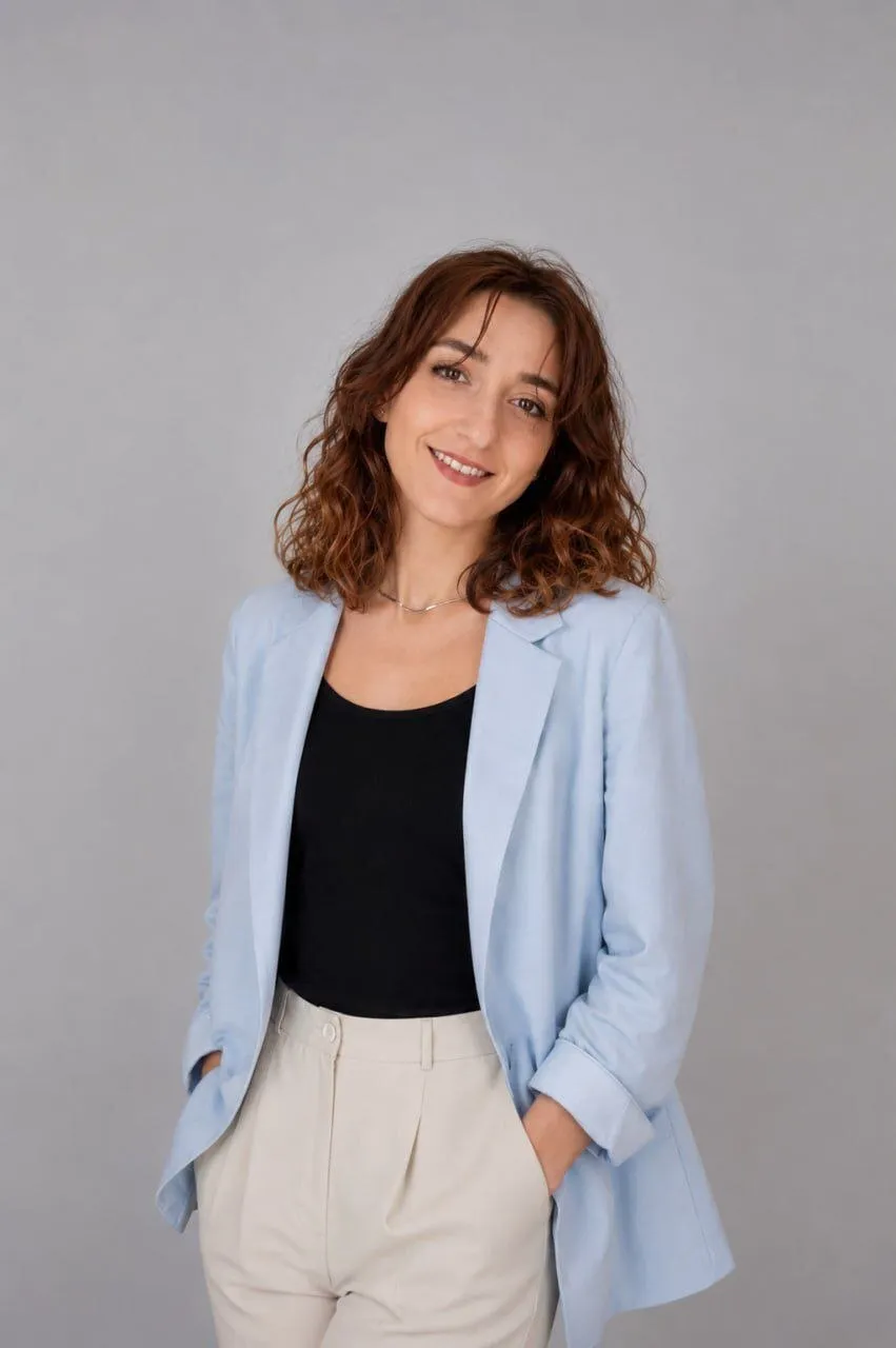 Frau mit kurzen braunen Haaren und schwarzem Blazer lächelt vor grauem Hintergrund.