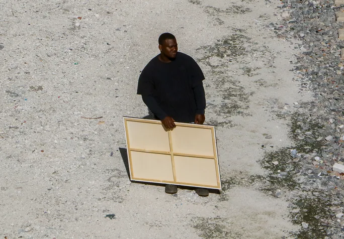 A man holding a blank canvas beside railroad tracks, from the VOUSCon 2027 campaign