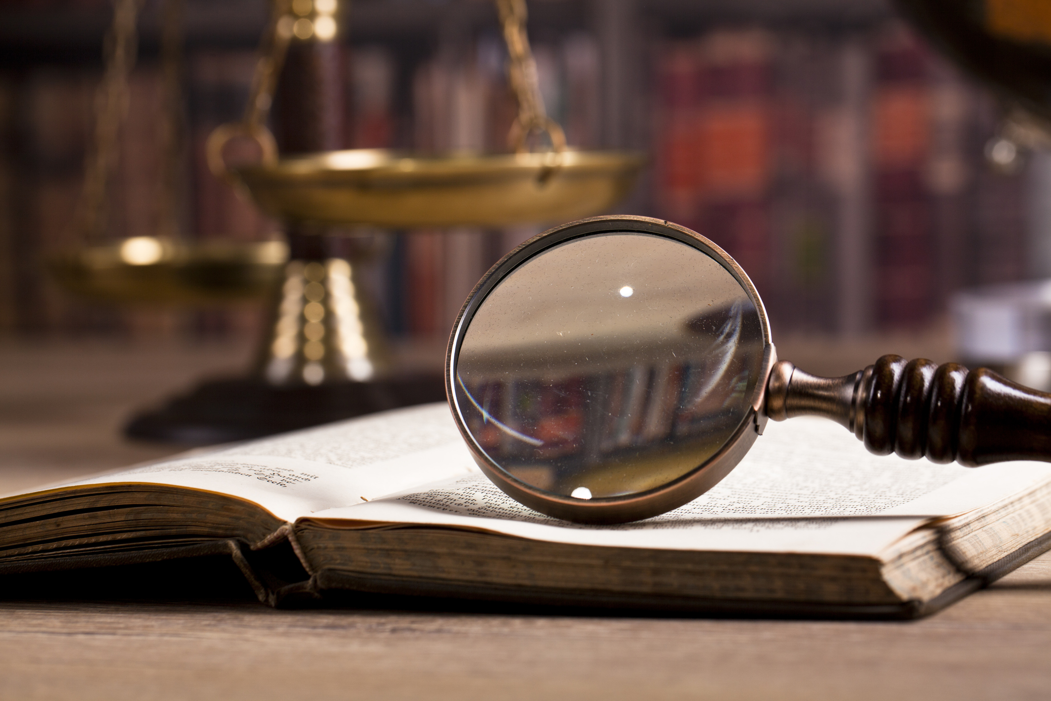 Middle-aged woman with glasses writing notes in a book at a large wooden table in a quiet library.