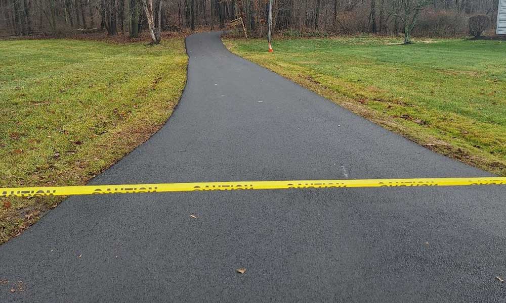 Freshly paved asphalt driveway leading to residential home with landscaped edges