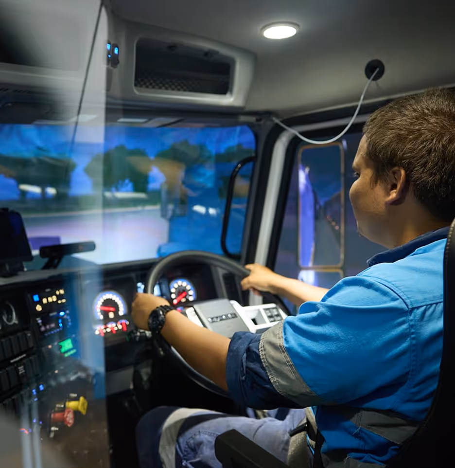 Man in blue uniform driving a large vehicle, holding the steering wheel with dashboard lights illuminated.