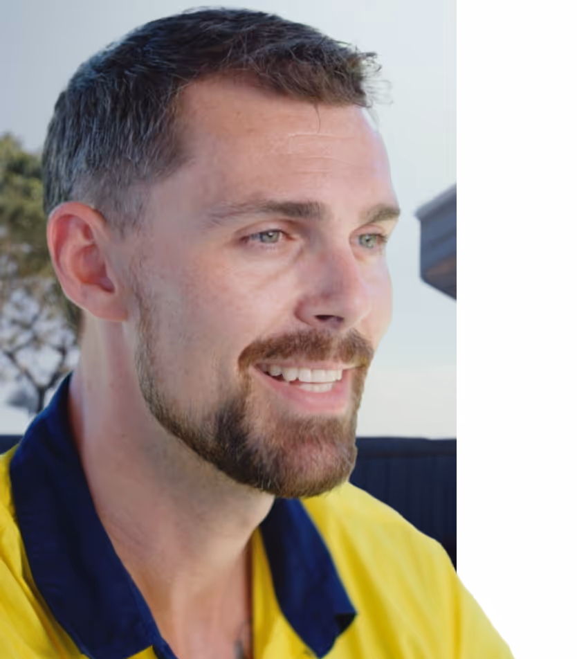 Close-up of a smiling man with short brown hair and a beard wearing a yellow shirt with a navy collar.