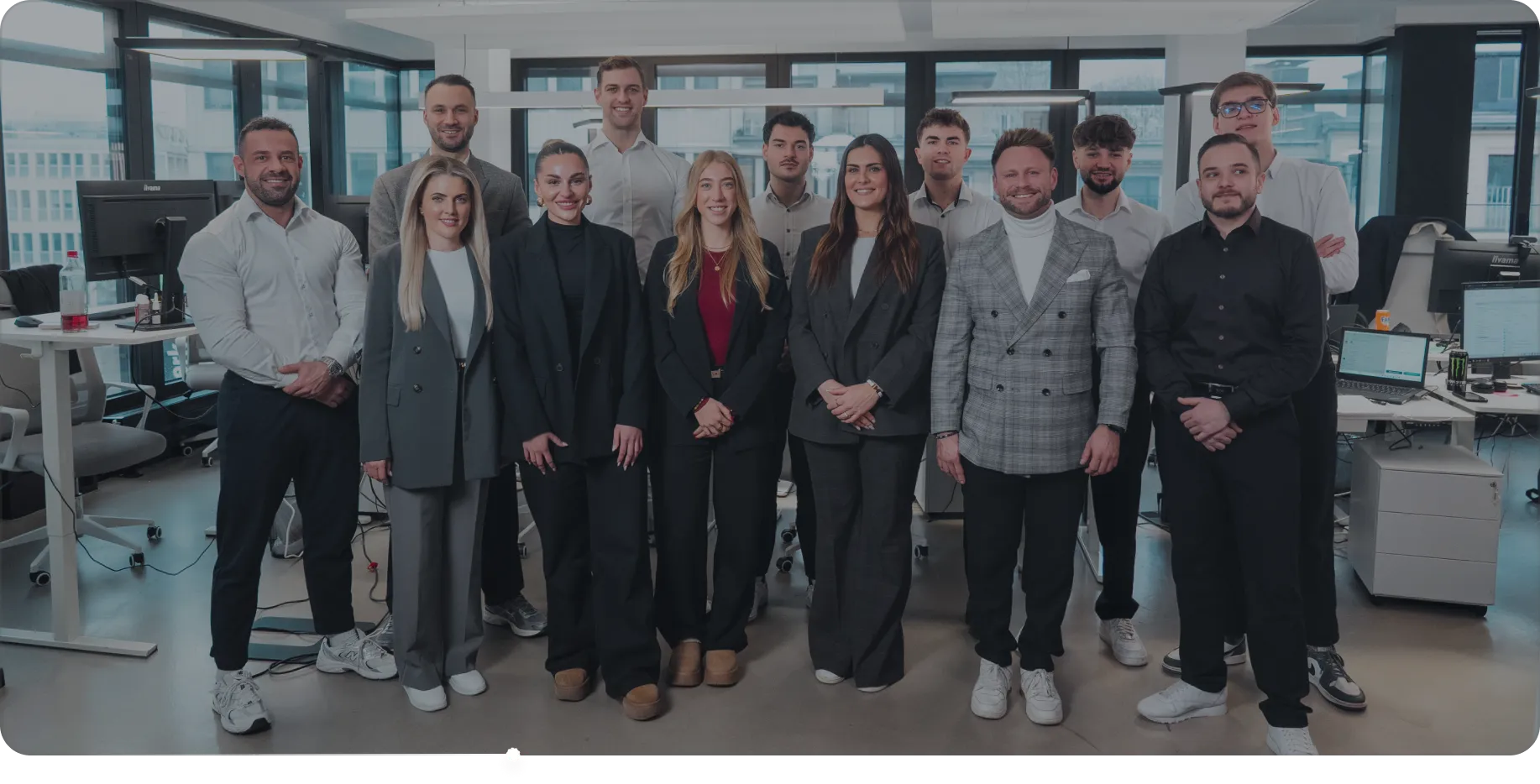 Moderne Bürofläche mit mehreren Arbeitsplätzen, Computern und Mitarbeitern, die an Schreibtischen arbeiten.