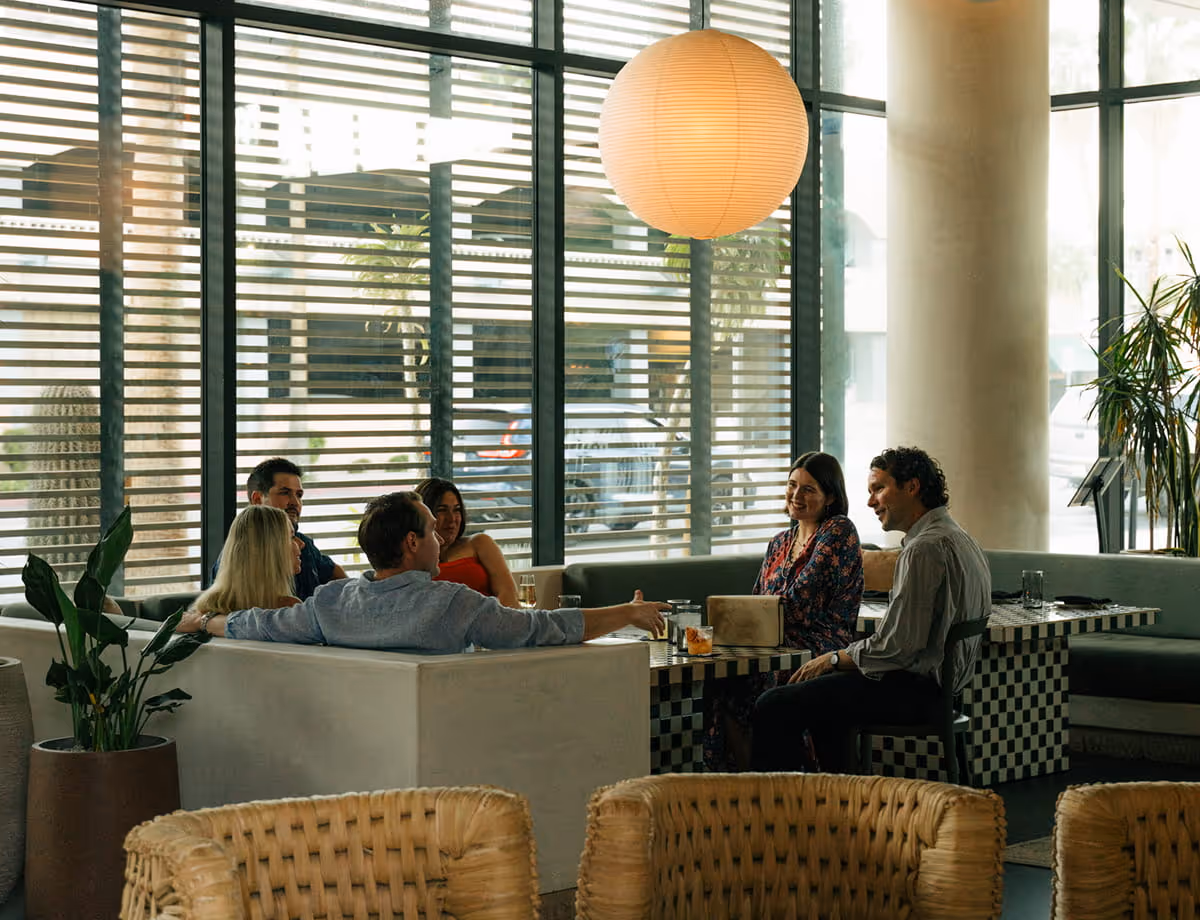 Group of friends enjoying cocktails and conversation in a modern restaurant lounge with large windows and paper lantern