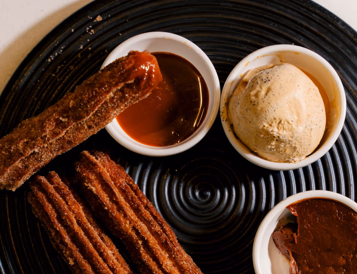 Churros coated in cinnamon sugar served on a black spiral plate with caramel sauce, coffee ice cream, and chocolate dip.