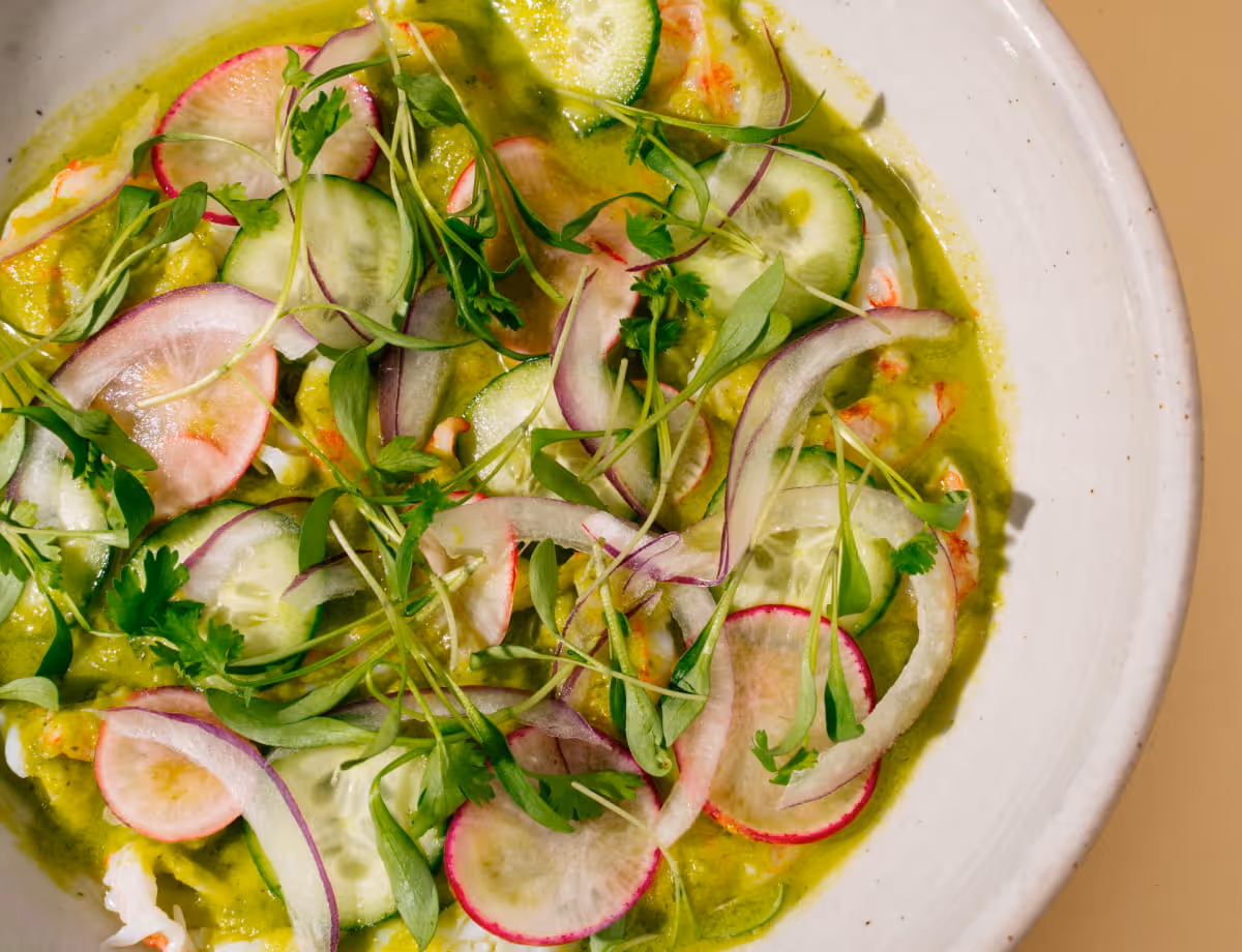 Vibrant green aguachile with shrimp, thinly sliced radishes, cucumber, red onion, cilantro, and microgreens in a ceramic