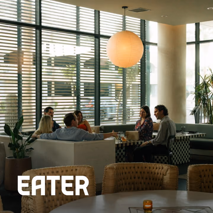 Diners enjoy drinks and conversation at a modern restaurant with large windows and a globe pendant light, via Eater