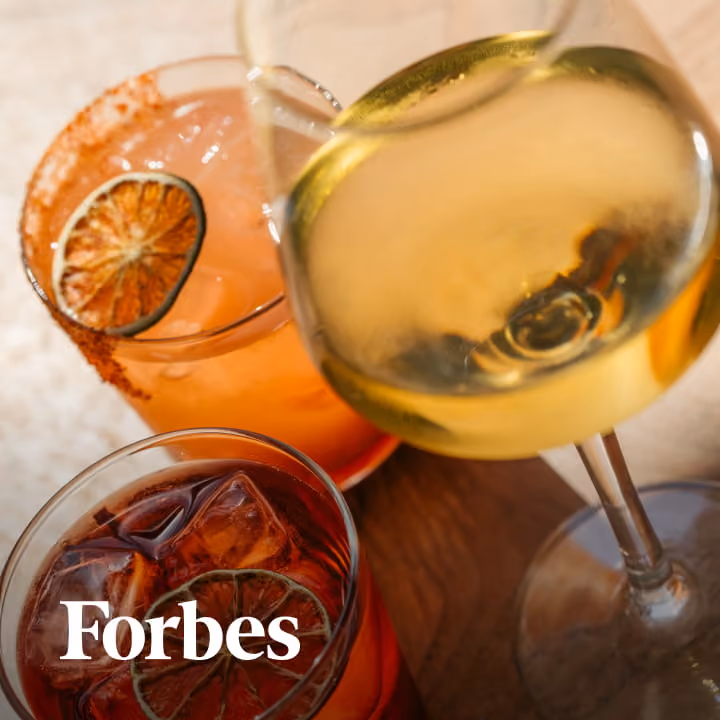Three craft cocktails including a pink paloma with dried citrus, a negroni on ice, and white wine, featured in Forbes.