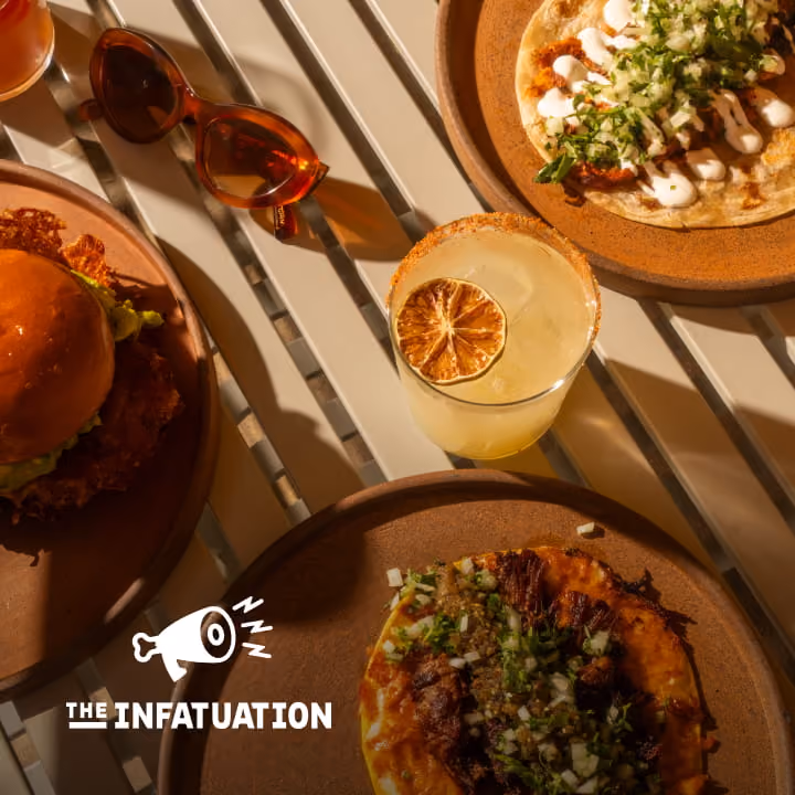 Overhead view of a burger, Mexican flatbreads, and a margarita with dried citrus on a slatted table by The Infatuation.