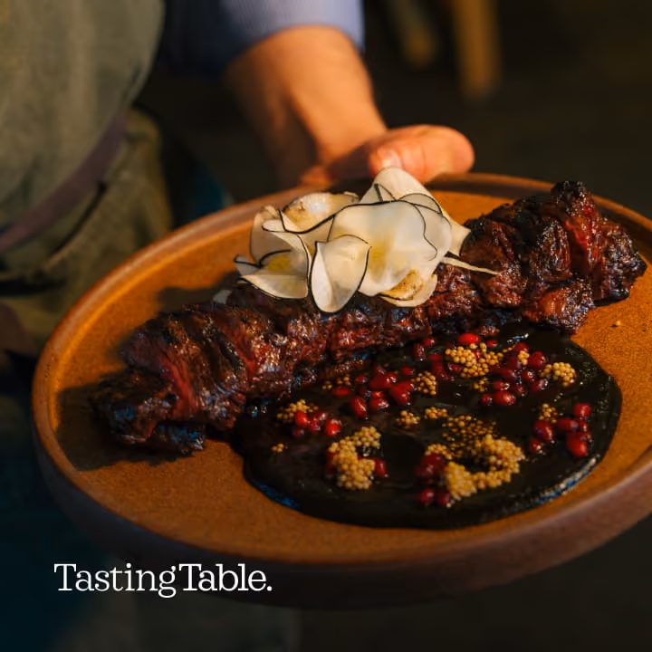 Grilled steak plated with black mole sauce, pomegranate seeds, mustard seeds, and shaved radish, featured in Tasting Table.
