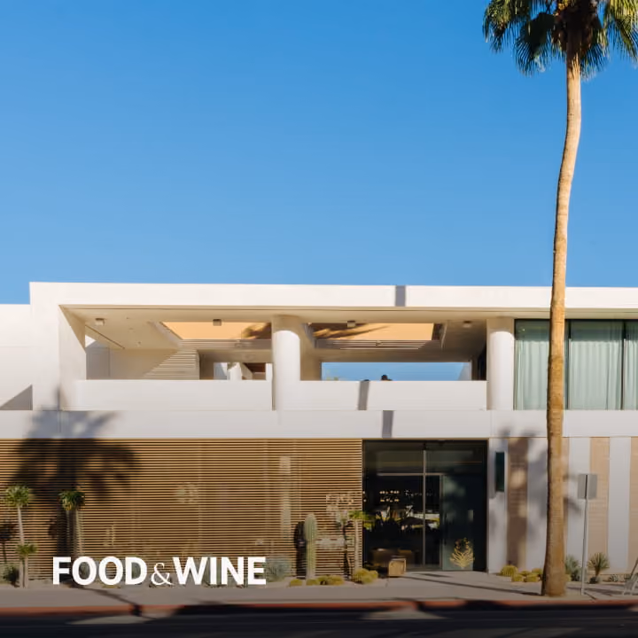 Modern white mid-century architecture building with palm tree and wooden slat facade under clear blue sky, featured in Food