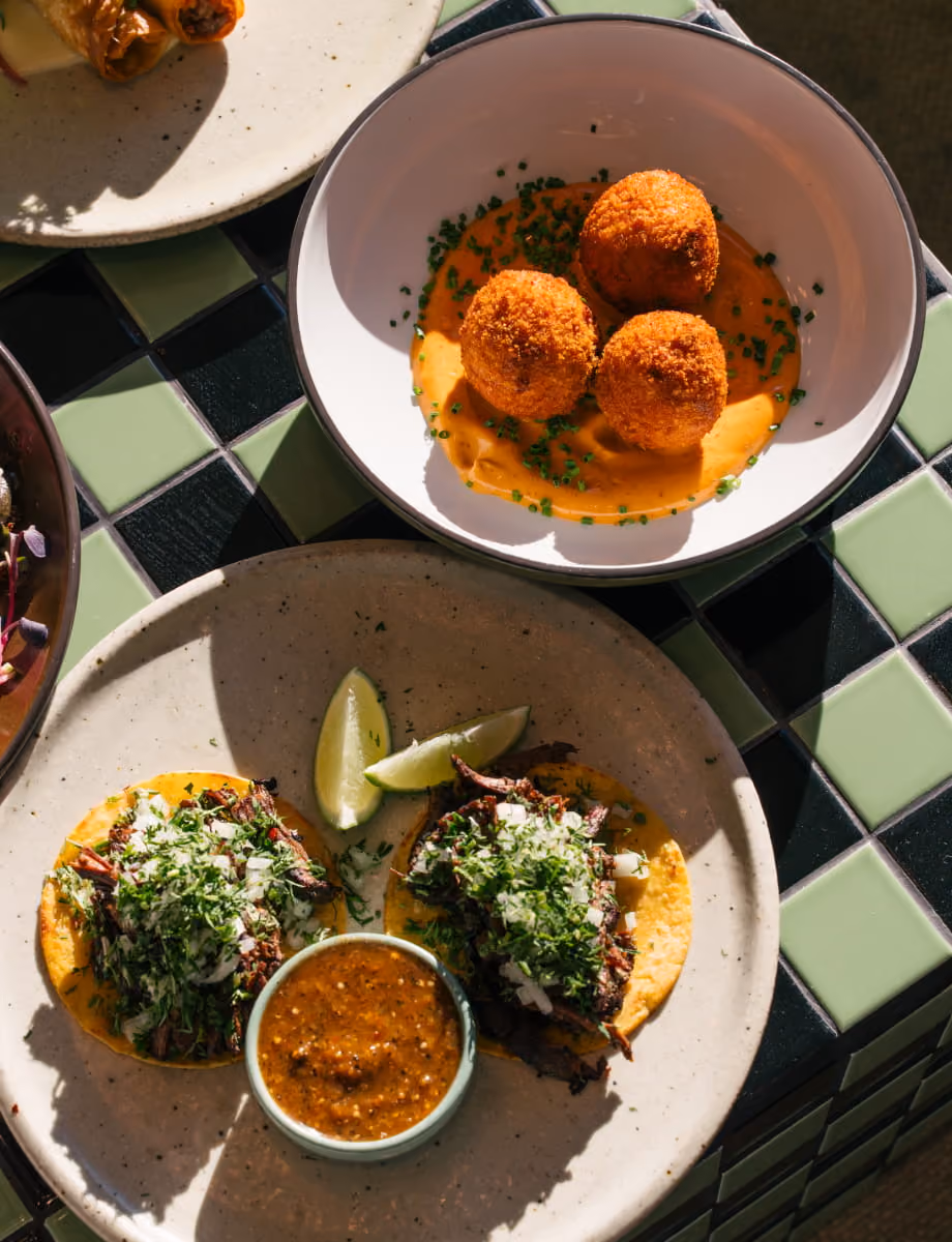 Crispy arancini in orange sauce and birria tacos with fresh cilantro and salsa on a checkered tile table