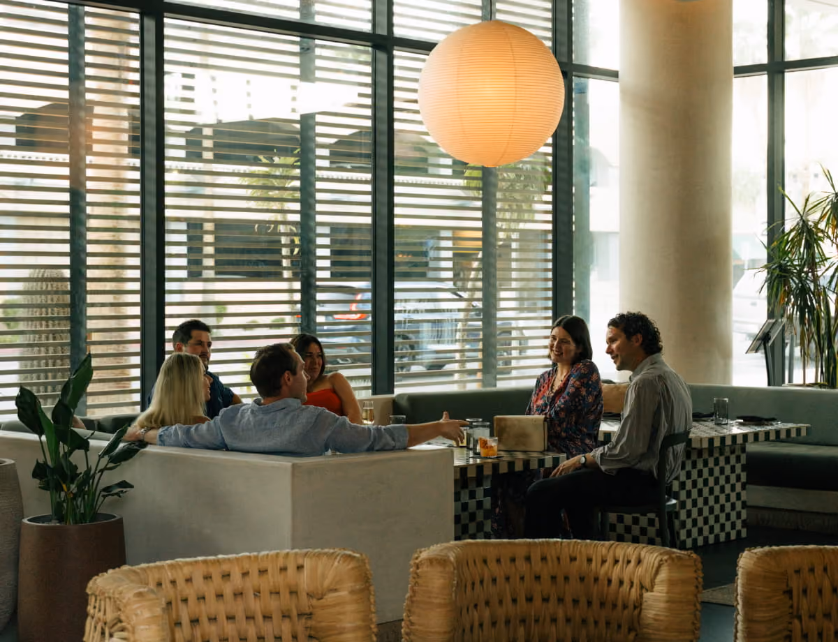 A group of friends enjoying cocktails and conversation in a modern lounge with large windows and stylish globe lighting