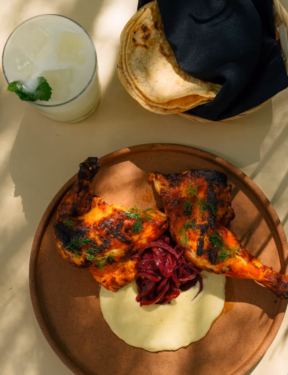 Grilled half chicken with pickled red onions, creamy sauce, and fresh dill, served with warm tortillas and a mint cocktail.