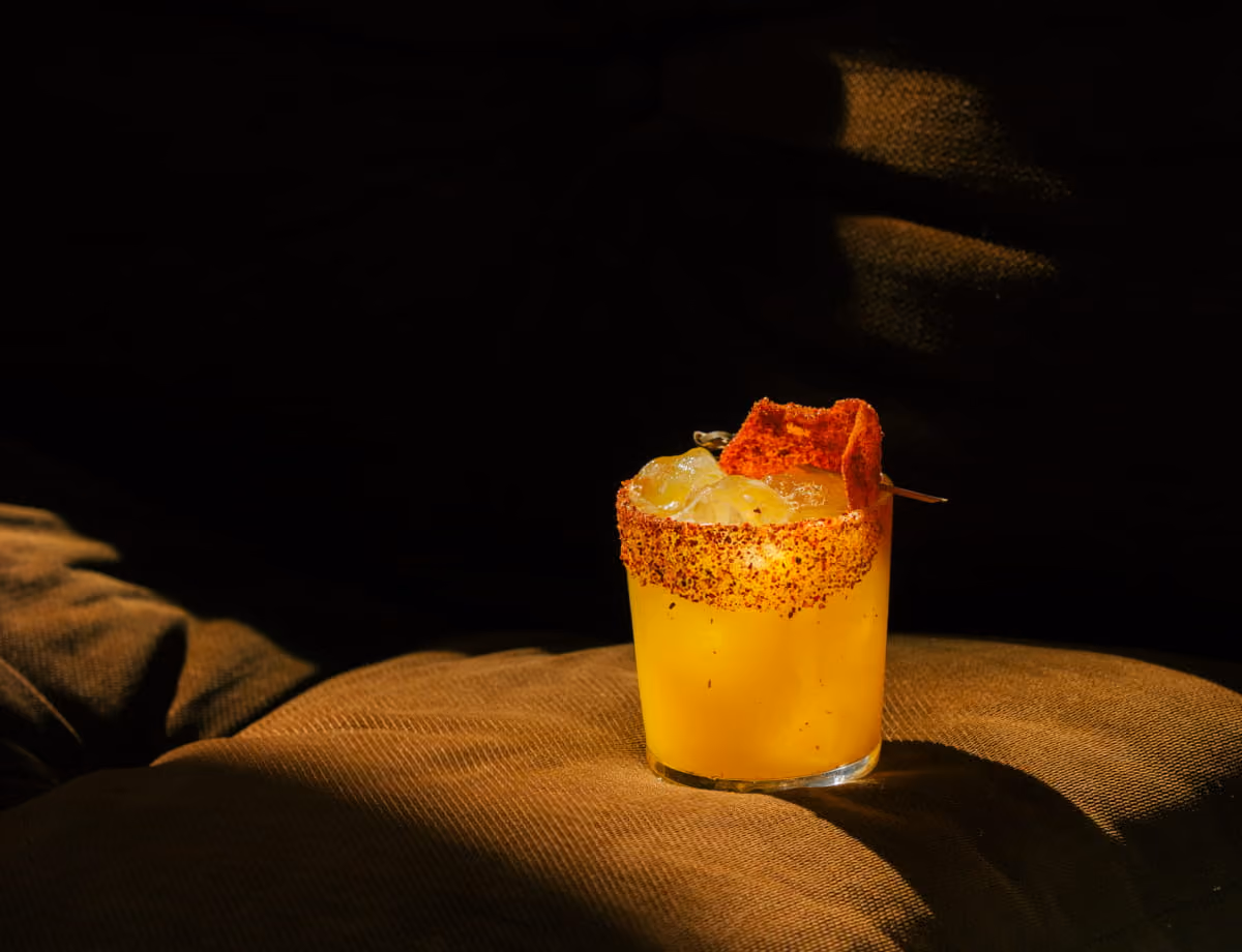Mango margarita cocktail with a chili-salt rim and dried fruit garnish, dramatically lit against a dark background