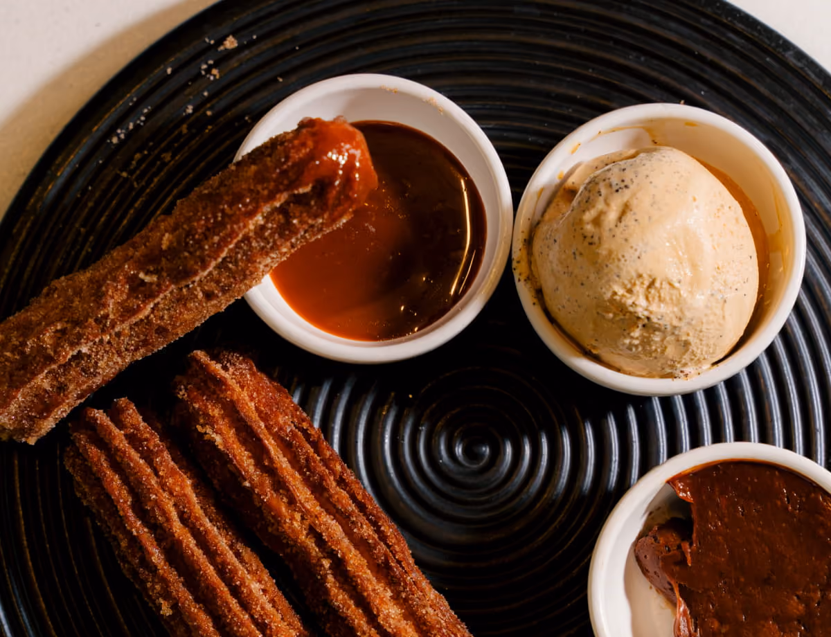 Cinnamon-sugar churros served with caramel dipping sauce, a scoop of coffee ice cream, and rich chocolate ganache.