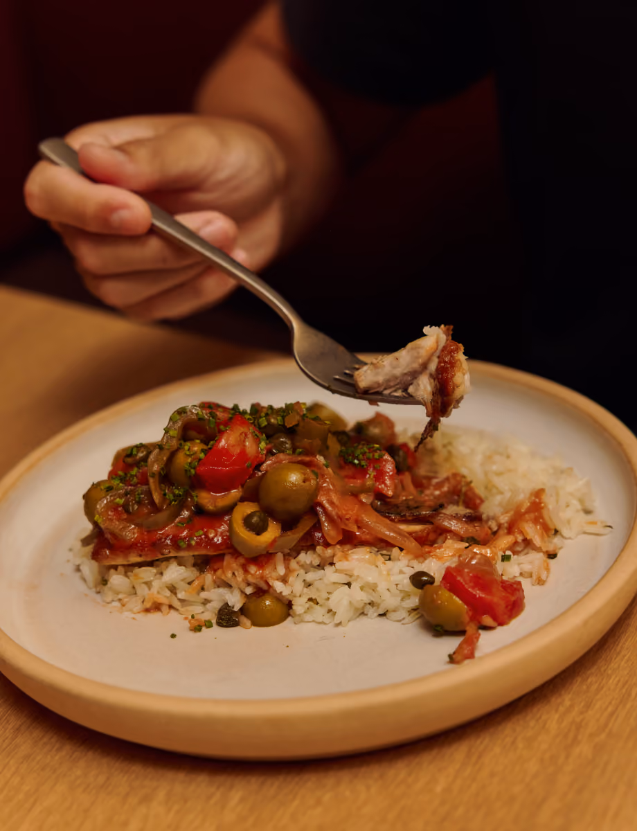 Slow-cooked shredded meat with green olives and tomatoes over rice, lifted on a fork.