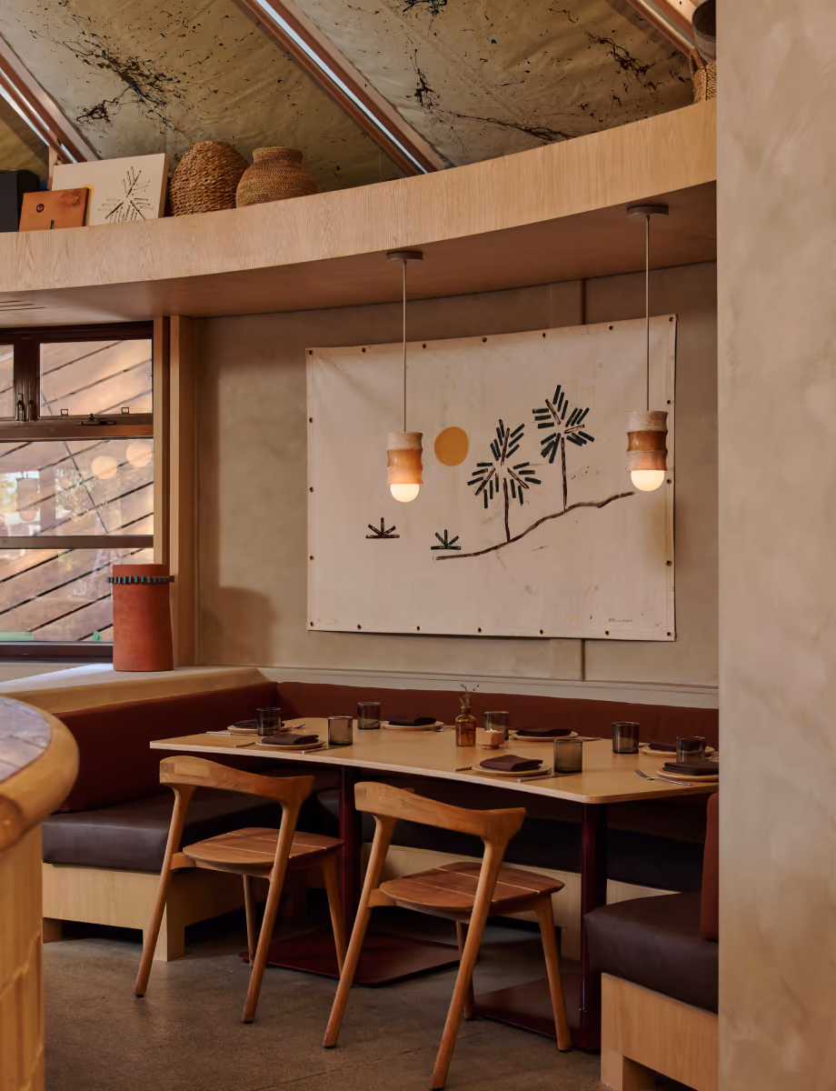 Booth dining nook with wooden chairs, pendant lights and a palm tree wall hanging beneath a curved ceiling.
