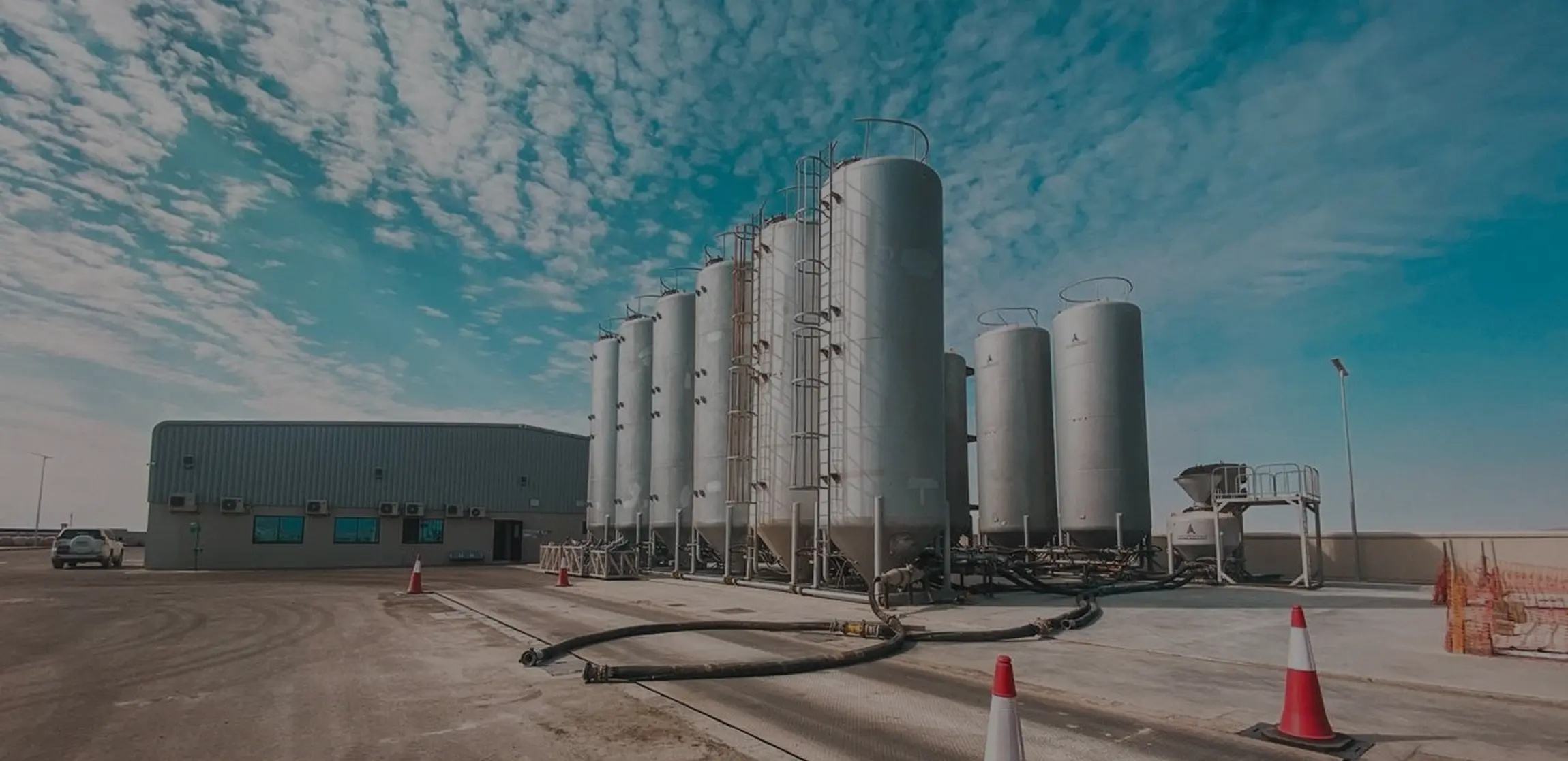 Row of tall silver industrial silos at a cement bulk plant under a blue sky with scattered