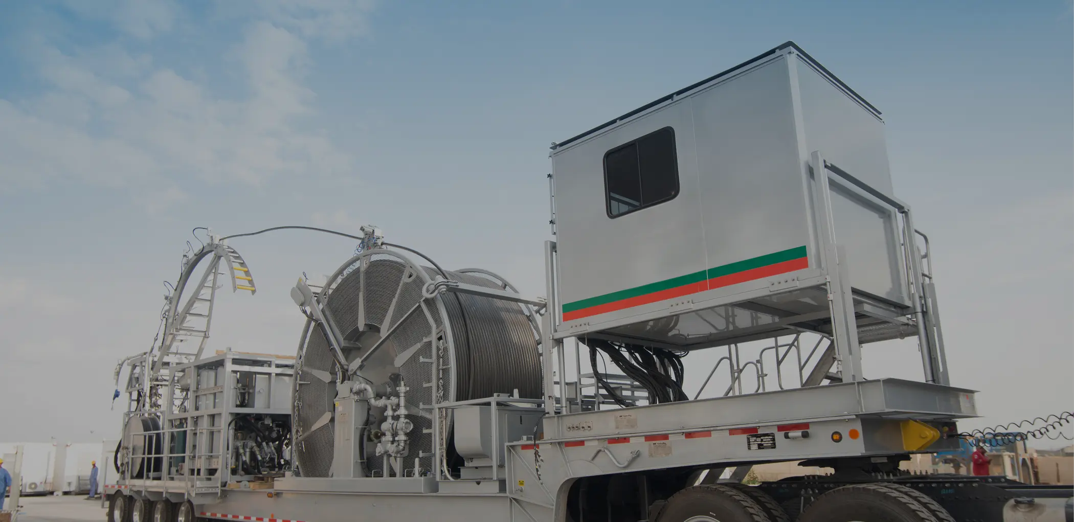 A wide shot of a specialized oilfield service trailer featuring a control cabin and a large coiled tubing reel unit.