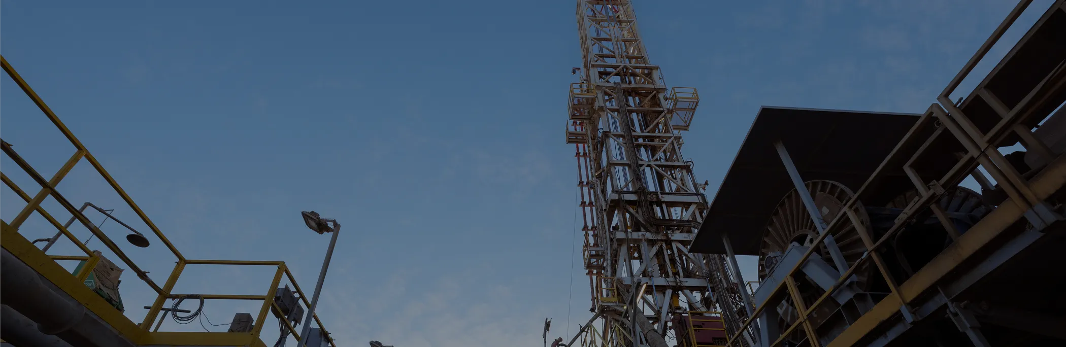 Low-angle view of a steel oil rig structure and yellow safety railings against a clear blue sky.
