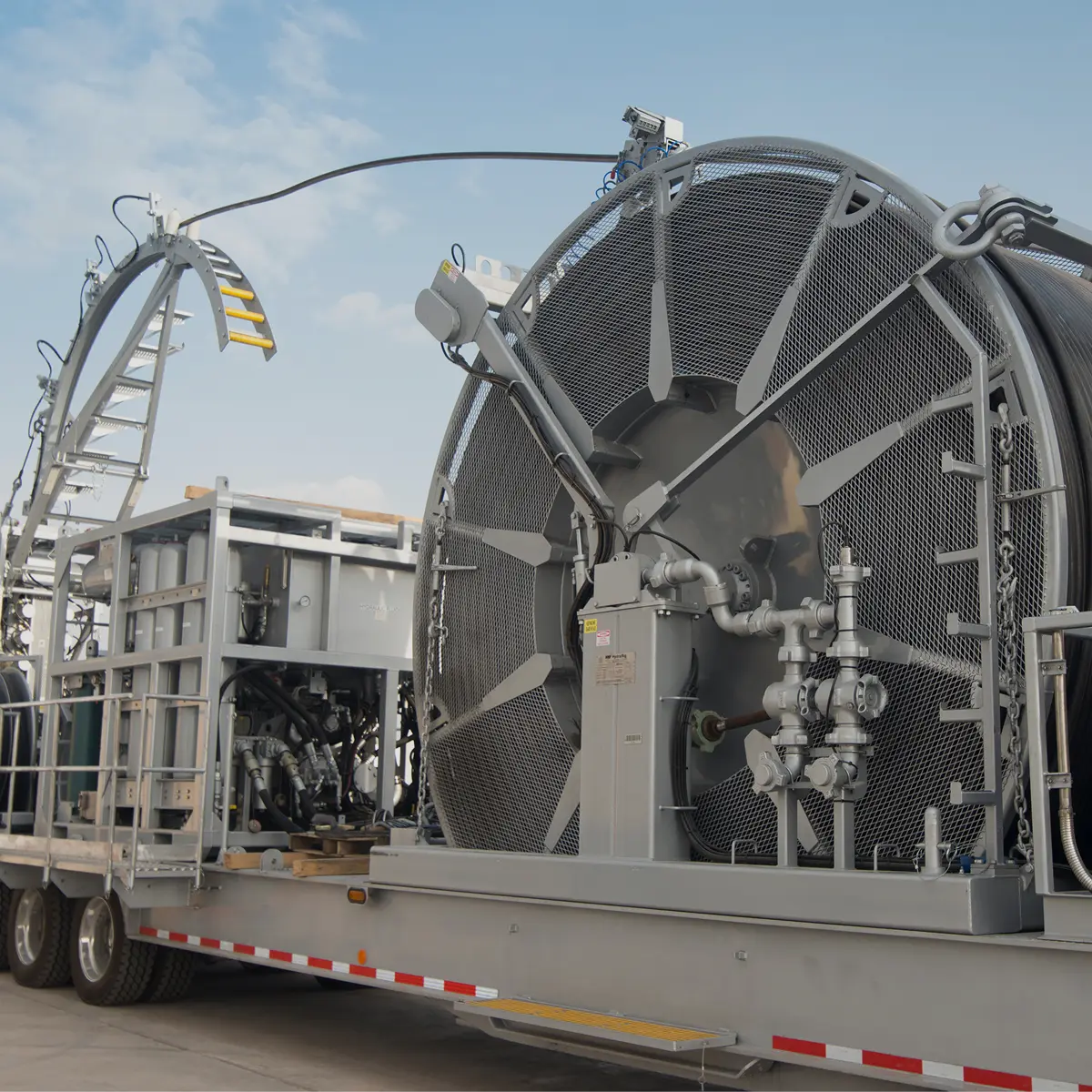 Close-up of a coiled tubing reel unit mounted on a trailer, showing the large metal drum and hydraulic piping.