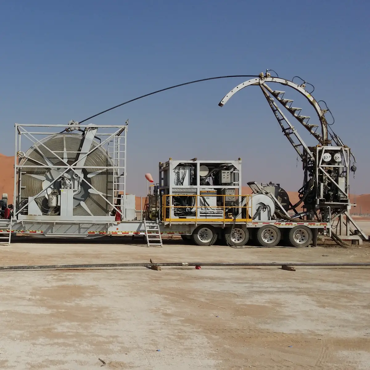 A full-length view of a coiled tubing unit on a trailer in a desert environment, with the tubing extending through an injector arch.