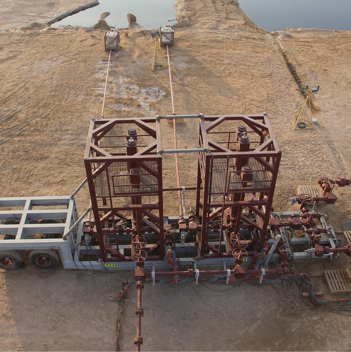 High-angle aerial view of an oil rig operation in the middle of vast orange sand dunes with large water storage pits.