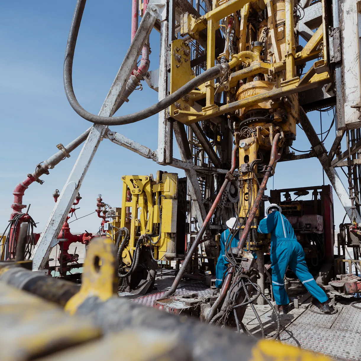 High-angle aerial view of an oil rig operation in the middle of vast orange sand dunes with large water storage pits.