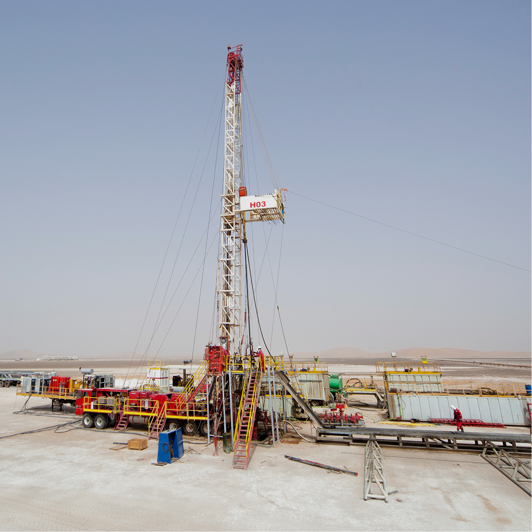 High-angle aerial view of an oil rig operation in the middle of vast orange sand dunes with large water storage pits.