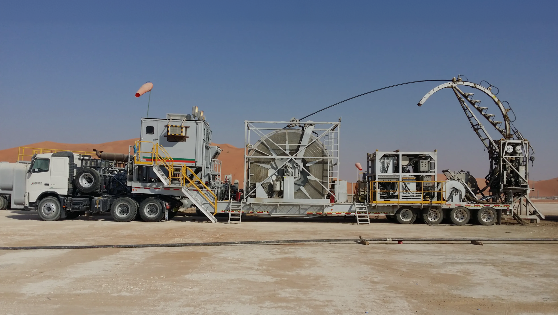 A wide view of a full coiled tubing unit mounted on a long trailer in a desert setting, with the tubing feeding through an injector arch.