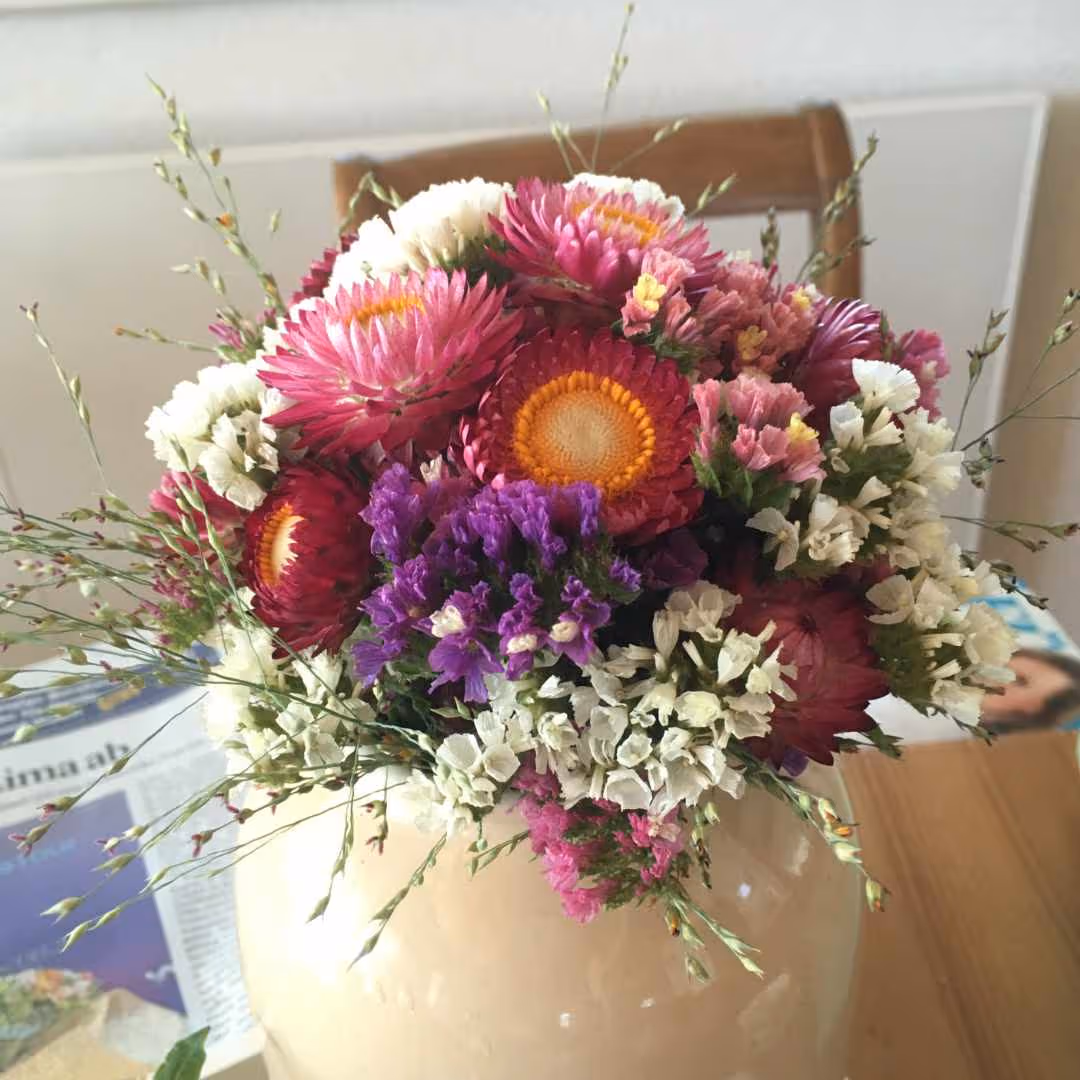Bunter Blumenstrauß mit pinken, weißen und violetten Blumen in einer Vase auf einem Holztisch.