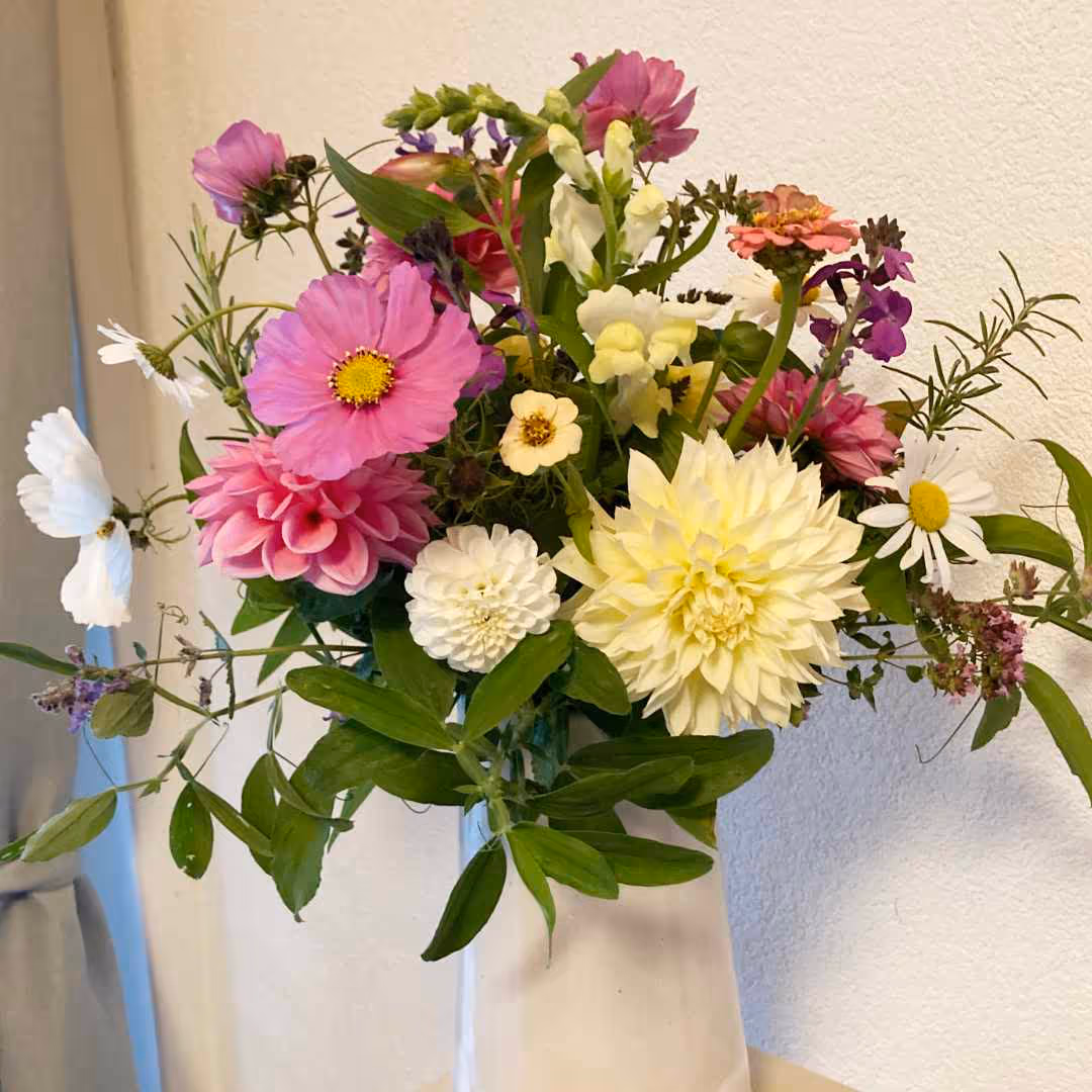 Bunter Blumenstrauß mit weißen, rosa und gelben Blüten in einer weißen Vase vor hellem Hintergrund.