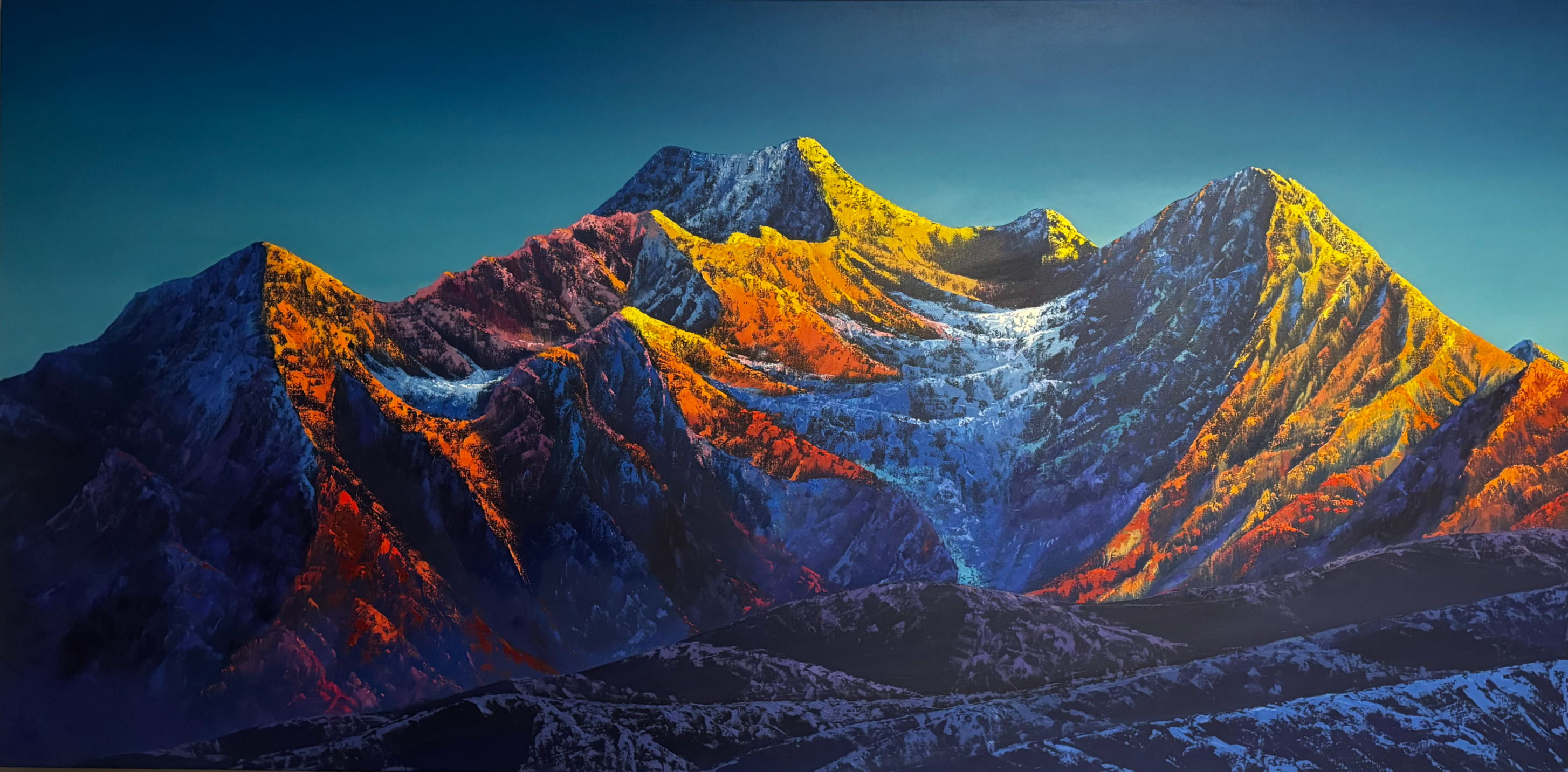 Mountain range illuminated by warm sunlight with contrasting shadows and snow patches under a clear blue sky.