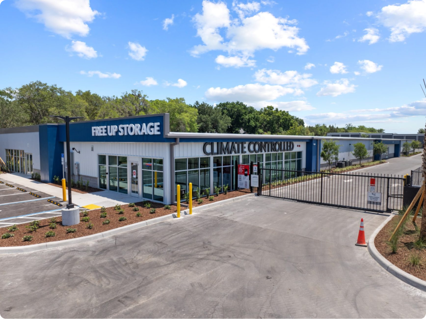 Exterior view of a Free Up Storage facility with climate-controlled units, secured by a gate under a blue sky with clouds.
