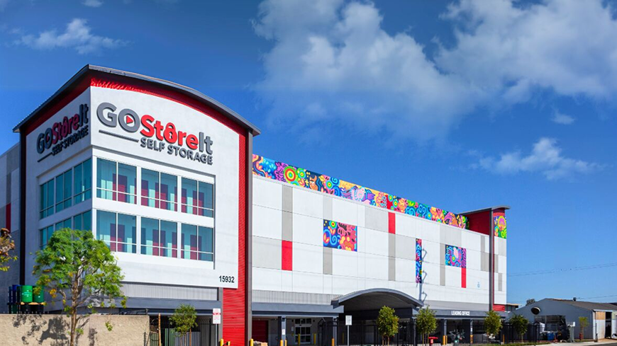 Modern GoStoreIt self storage building with colorful abstract murals under a bright blue sky.