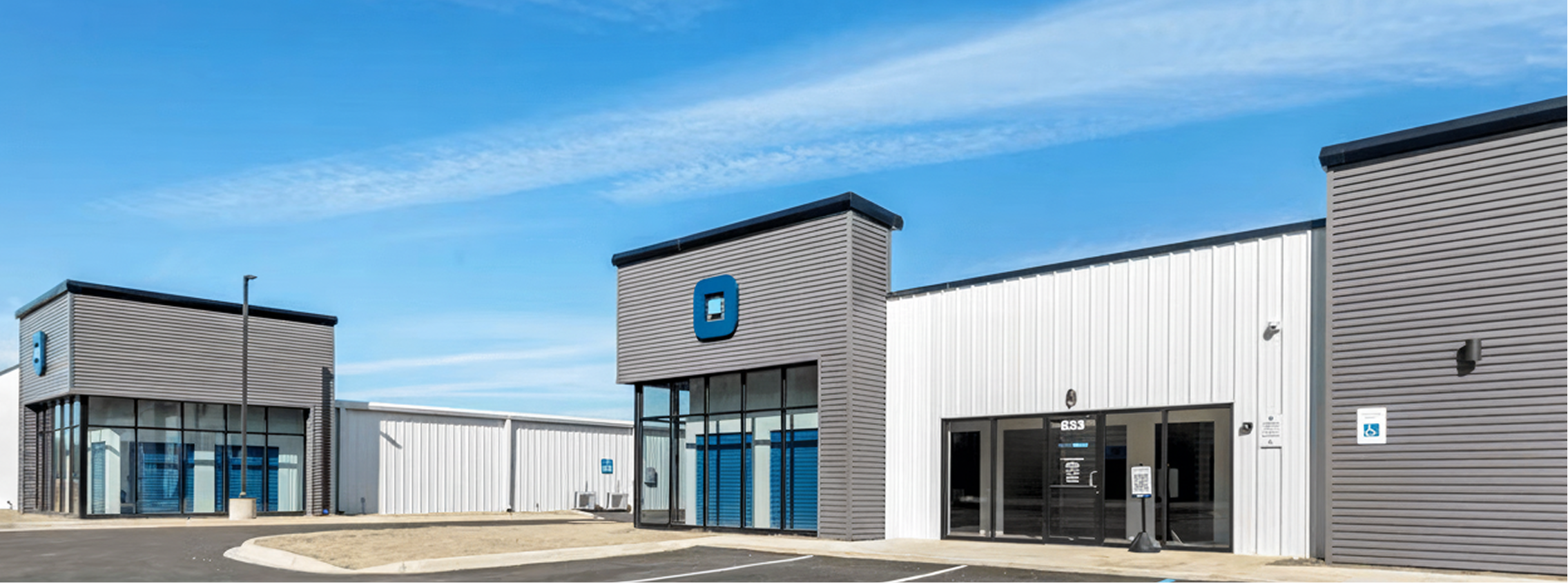 Modern self-storage facility with gray and white exterior, large windows, and blue storage unit doors.
