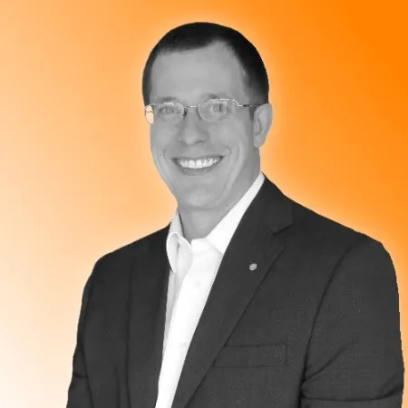 Smiling man with glasses wearing a dark suit and white shirt against an orange gradient background.