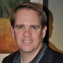 Portrait of a man with short light brown hair wearing a dark jacket and striped shirt.