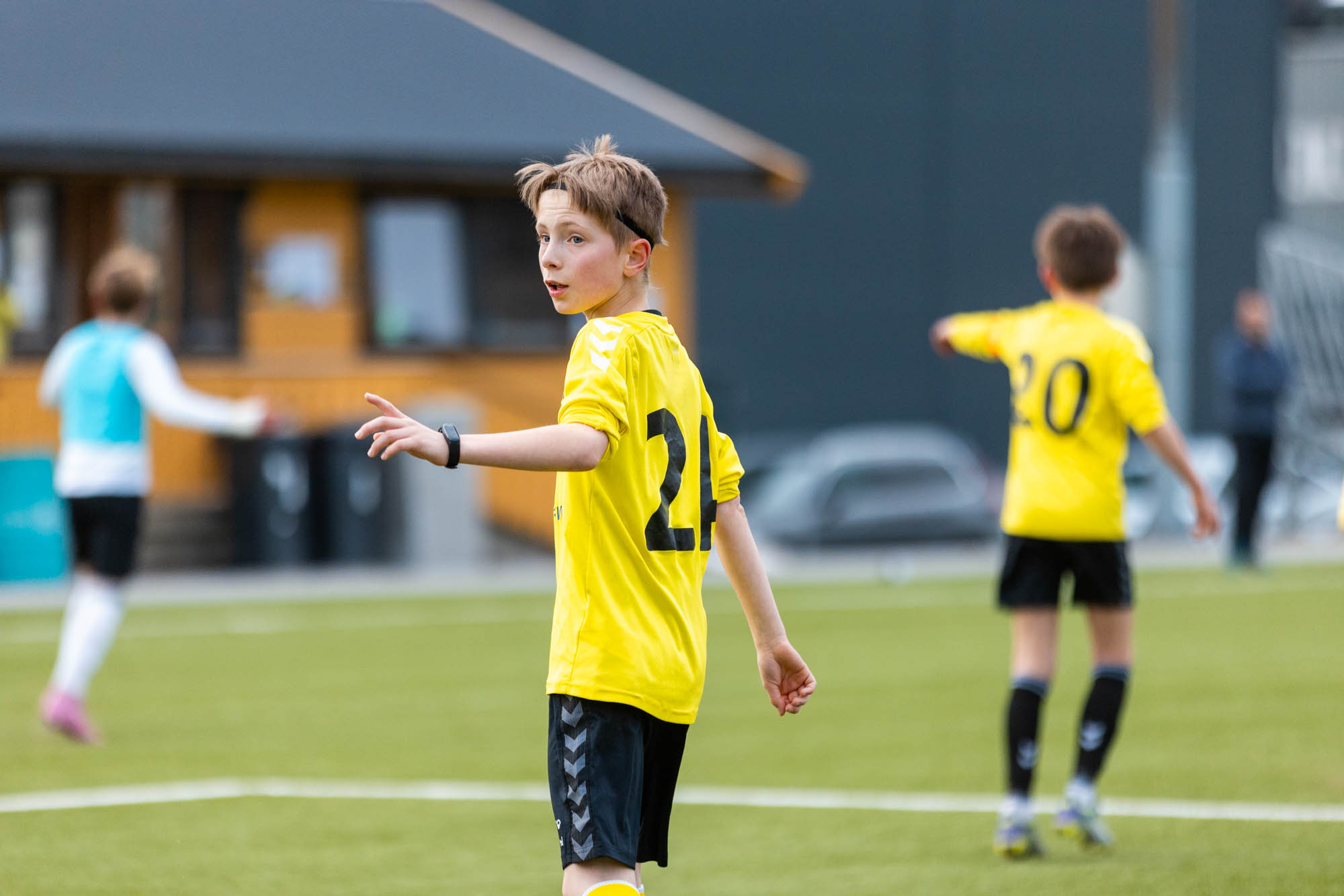 Ung gutt i gult fotballdrakt peker på banen under en kamp på kunstgress.