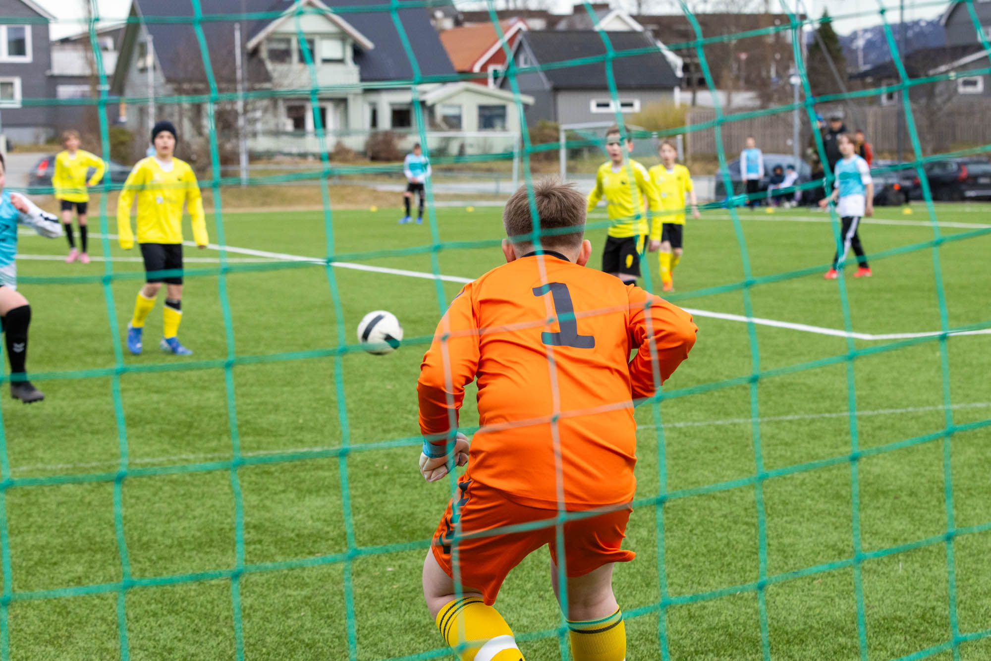 Ung målvakt i oransje drakt forbereder seg på å redde et straffespark på fotballbane.