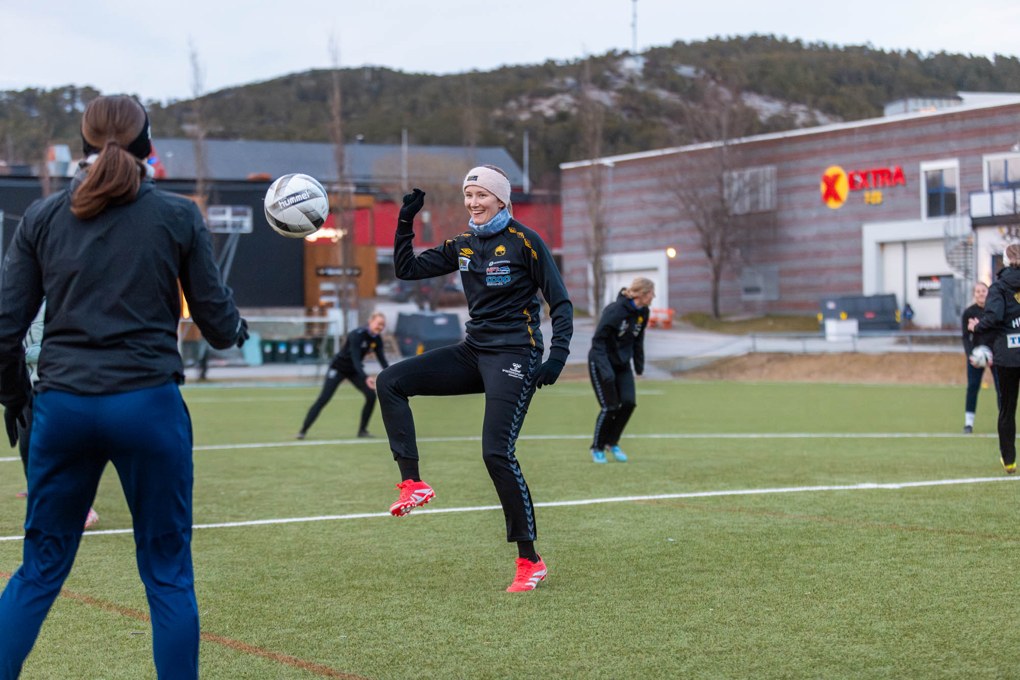Kvinnelige fotballspillere trener utendørs på kunstgress, én sparker ballen med røde sko.