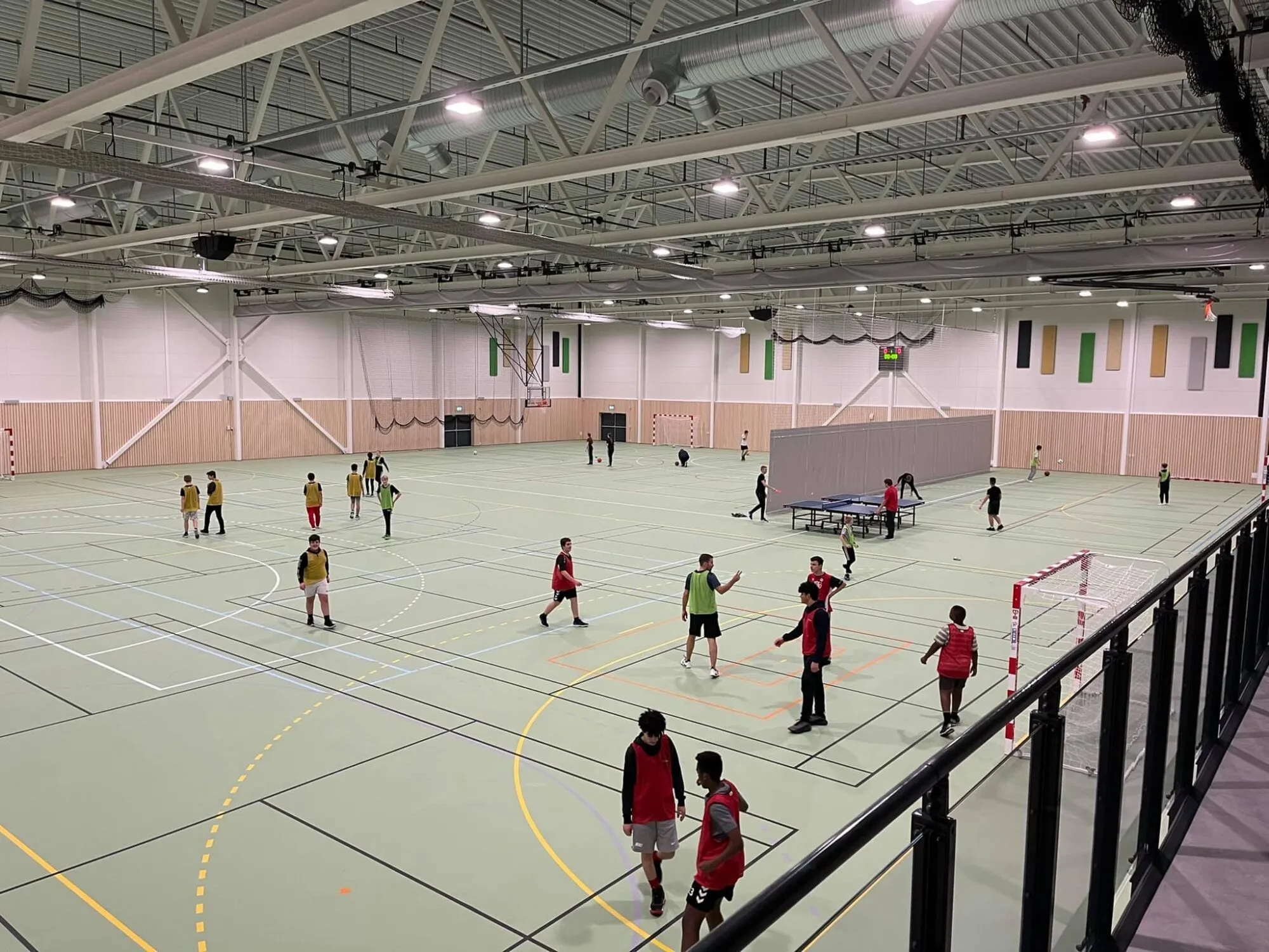 Innendørs flerbruks idrettshall med flere grupper ungdom som spiller ulike sporter og aktiviteter.