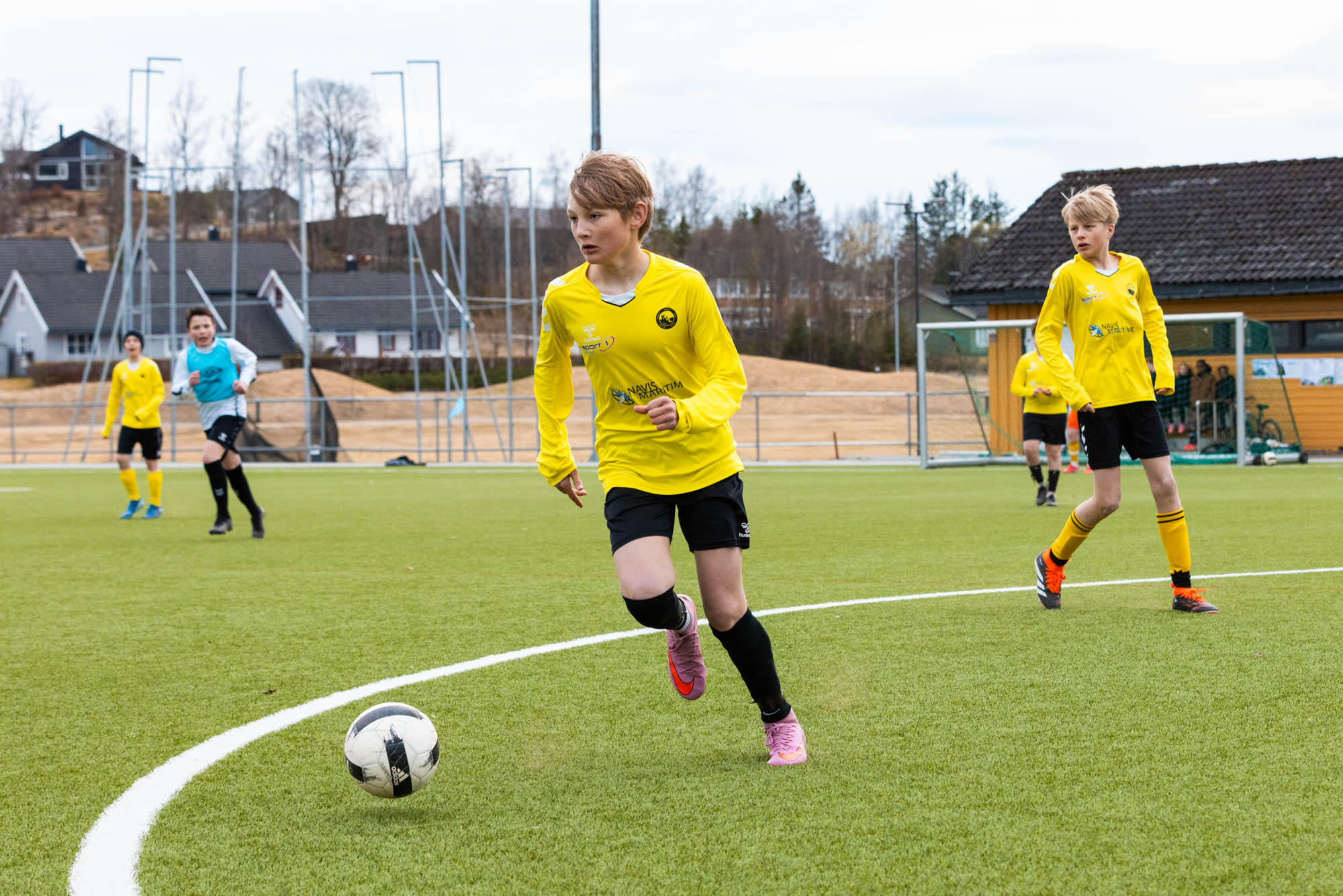 Ung gutt i gul drakt løper mot en fotball på grønn gressbane under kampen.