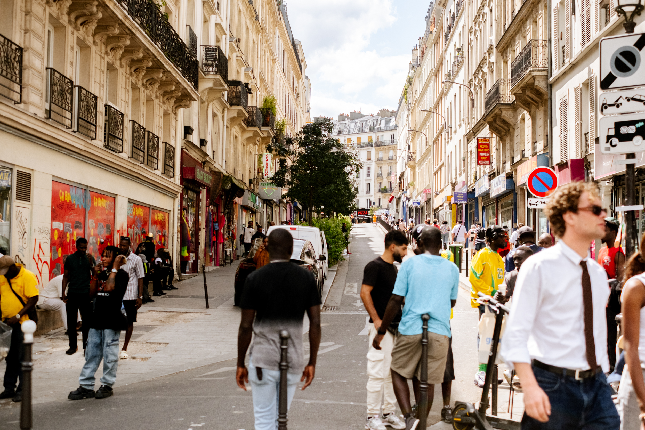 Rue animée à Paris avec plusieurs piétons marchant entre des bâtiments haussmanniens.