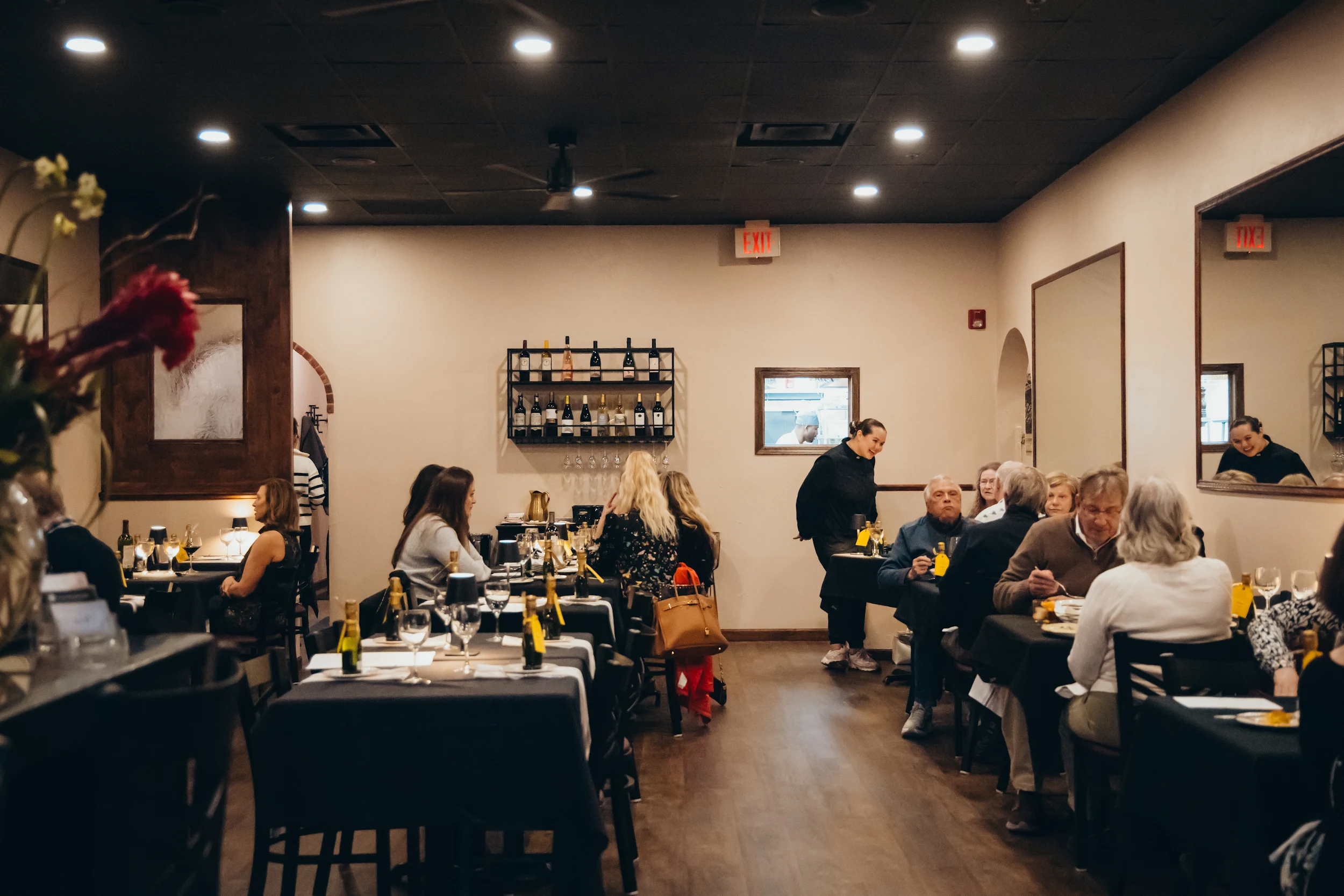 Interior of a busy restaurant with diners seated at tables and a waiter serving customers.