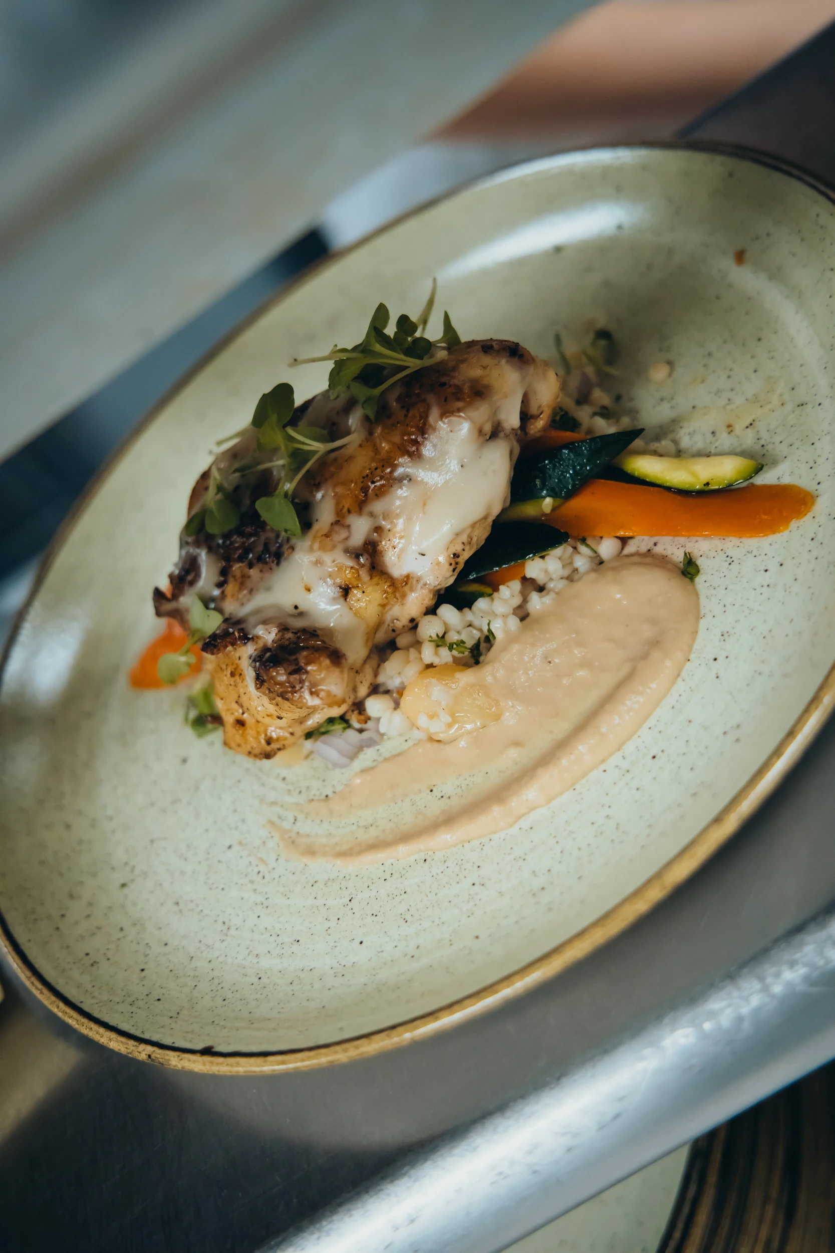 Plate with grilled chicken topped with melted cheese, served with vegetables, grains, and a creamy sauce.