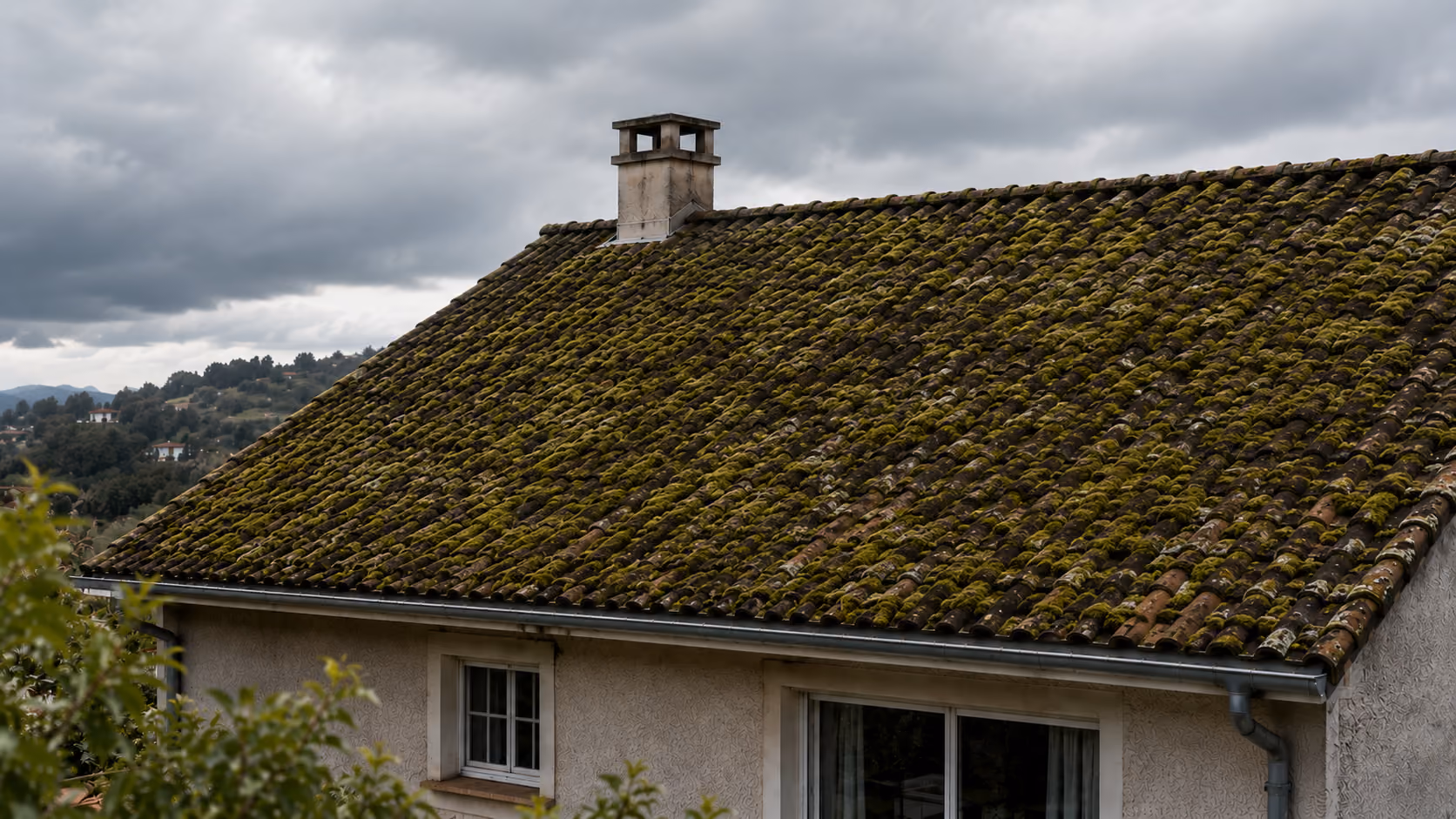 Toit de maison avec tuiles en terre cuite rouge et gouttière en métal sous un ciel bleu avec quelques nuages.