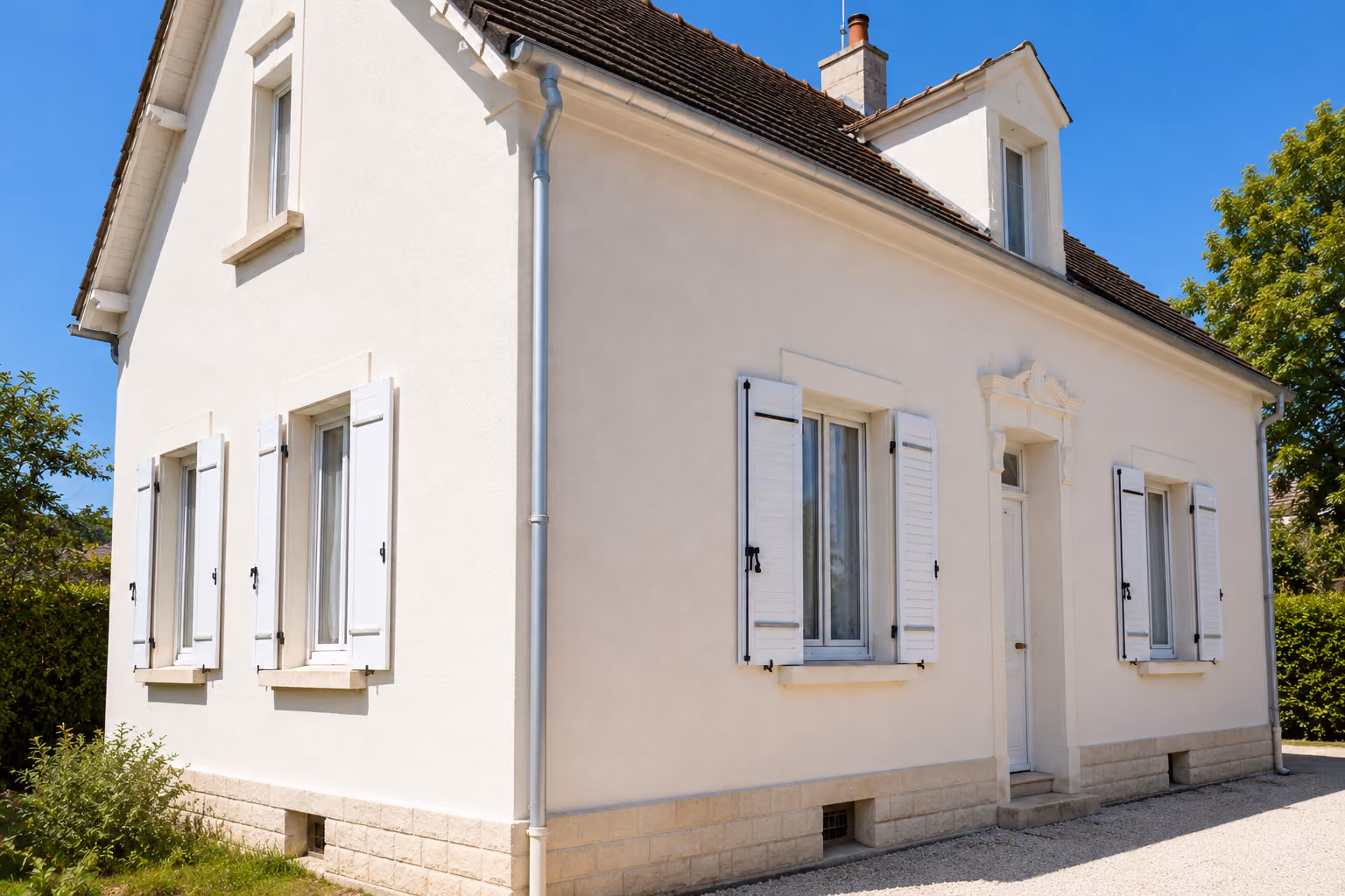 Toit de maison avec tuiles en terre cuite rouge et gouttière en métal sous un ciel bleu avec quelques nuages.