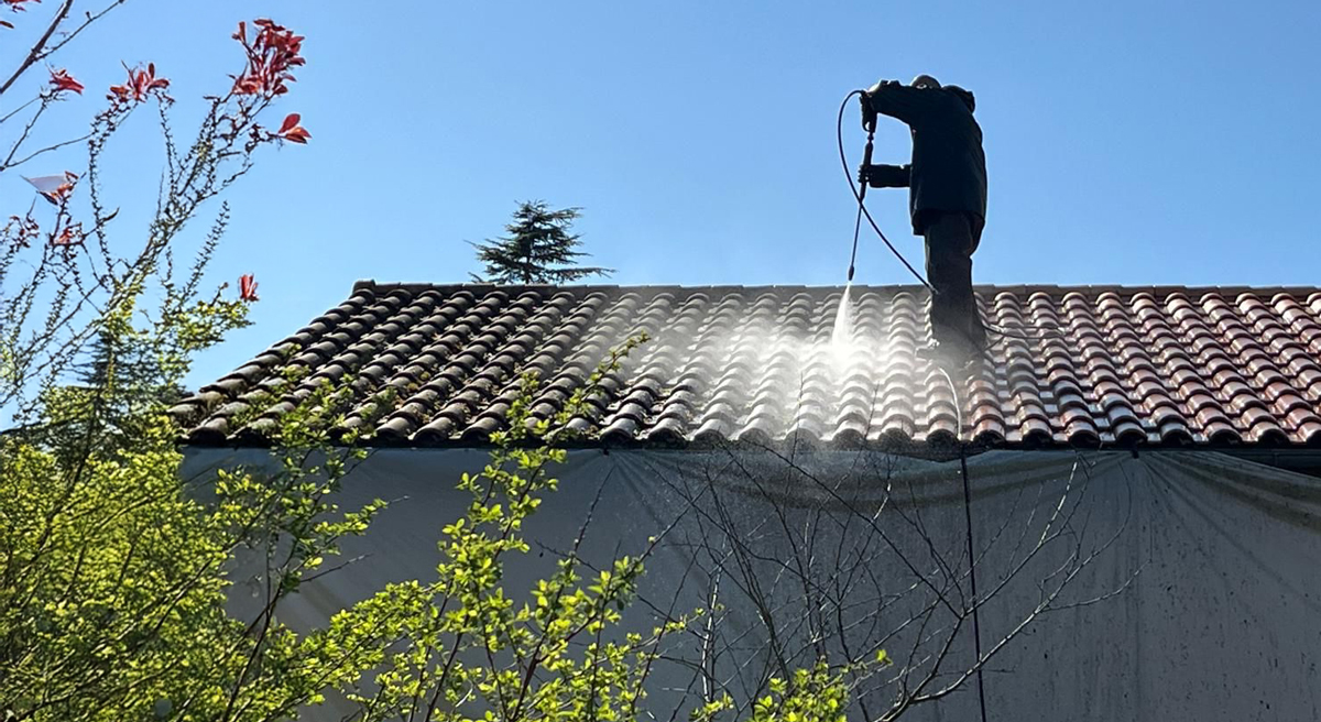 Couvreur nettoyant une toiture à haute pression.